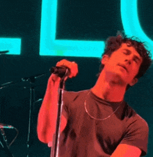a man singing into a microphone on a stage in front of a neon sign that says l
