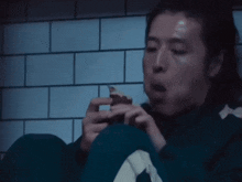 a man in a green jacket with the letter a on it is eating something