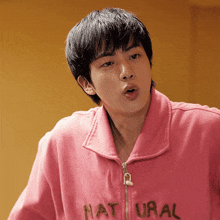 a young man wearing a pink sweatshirt that says natural on it