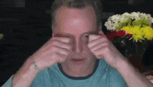 a man in a blue shirt is covering his eyes with his hands
