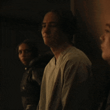 a man in a white shirt sits in a dark room with two other people
