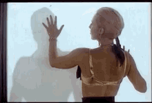 a woman in a bra is standing in front of a window and touching the glass with her hand .