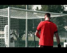 a man in a red shirt stands behind a soccer goal