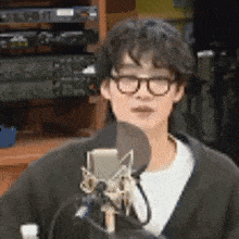a man wearing glasses is standing in front of a microphone in a room .