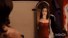 a woman is looking at herself in a mirror while wearing a red dress .