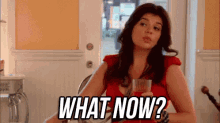 a woman is sitting at a table holding a glass of wine and asking , `` what now ? ''