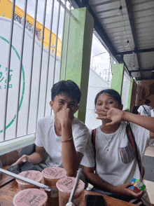a boy and a girl are sitting at a table with cups of bubble tea on the table