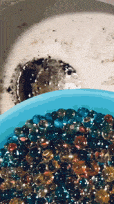 a blue bowl filled with colorful water beads sits next to a sink drain