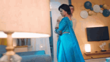 a woman in a blue saree stands in a living room