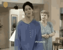 a woman in a blue shirt stands next to an older woman in a living room .