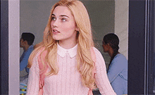 a woman in a pink sweater and white collar is standing in front of a window .