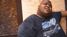 a very fat man is sitting in front of a brick wall wearing a black shirt .