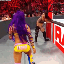 a woman with purple hair is standing next to another woman in a wrestling match in front of a crowd .
