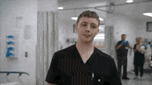 a young man in scrubs is standing in a hospital hallway and smiling .