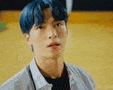 a man with blue hair and a black shirt looks at the camera