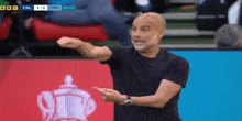 a man in a black shirt is standing on a soccer field giving instructions to his players .