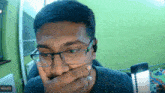 a man wearing glasses and ear buds is covering his mouth in a zoom call with niveth