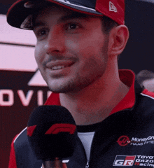 a man wearing a hat and a jacket that says toyo gazo racing is talking into a microphone