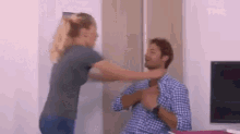 a man and a woman are fighting in a living room . the woman is hitting the man in the face .