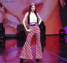 a woman wearing striped pants and a white top is standing on a stage .