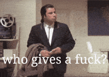 a man in a suit is standing in front of a sign that says who gives a fuck ?