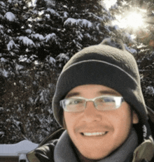 a man wearing glasses and a beanie is smiling for the camera