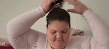 a woman is putting her hair in a bun while sitting on a bed .