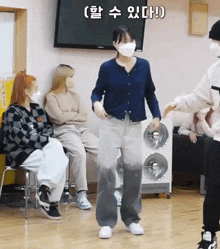 a woman wearing a face mask is dancing in front of a group of people wearing masks