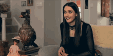 a woman in a black dress sits in front of a stuffed duck