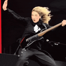 a man in a black jacket is playing a black guitar