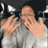 a woman wearing glasses and a hoodie covering her face with her hands
