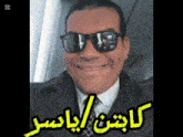 a man wearing sunglasses and a suit is smiling with arabic writing on the bottom