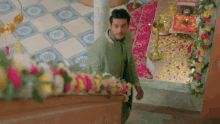 a man in a green jacket is standing in a room with flowers and candles on the floor