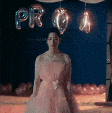 a woman in a pink dress is standing on a stage in front of balloons .