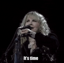 a woman singing into a microphone with the words " it 's time " next to her