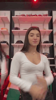 a woman in a white shirt is standing in front of a wall of shelves .