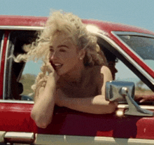 a woman is leaning out of a car window and smiling .