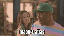 a man and a woman are standing next to each other and the man is wearing a green hat that says mack & atlas on it