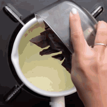 a person is pouring chocolate pieces into a pot of liquid