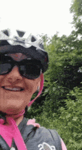 a woman wearing a helmet and sunglasses is smiling while riding a bike in the woods .