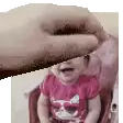 a baby is sitting in a high chair with a person 's hand over her head .