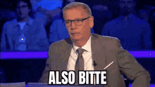 a man in a suit and tie is sitting in front of a microphone and says also bitte .