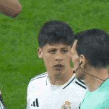 a soccer player wearing a white adidas jersey is talking to an umpire