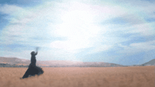 a woman in a long black dress stands in a field with her arms in the air