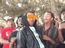 a group of young men are dancing in a park with a man wearing a hoodie covering his eyes