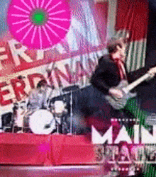 a man is playing a guitar on a stage while a drummer plays drums behind him .