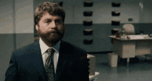 a man with a beard wearing a suit and tie is standing in an office