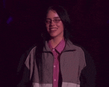 a woman wearing glasses and a striped shirt smiles in the dark