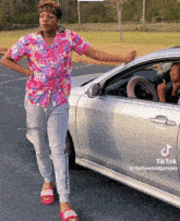 a woman in a pink shirt is standing next to a silver car with tiktok written on the bottom
