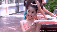 a young girl in a pink dress is smiling and holding her hands together